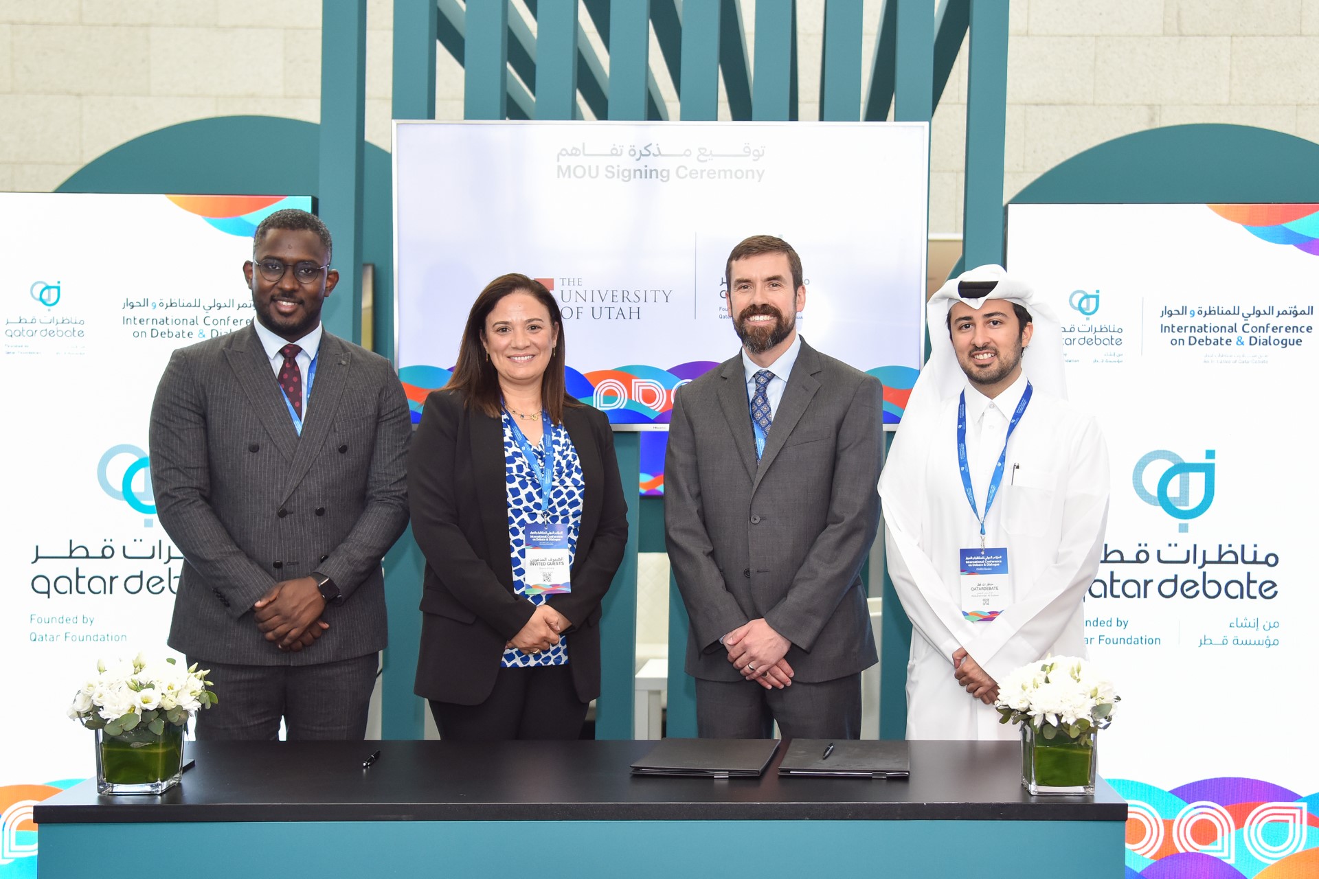 A group of 4 people stand in a line behind a blue table with a black top. 