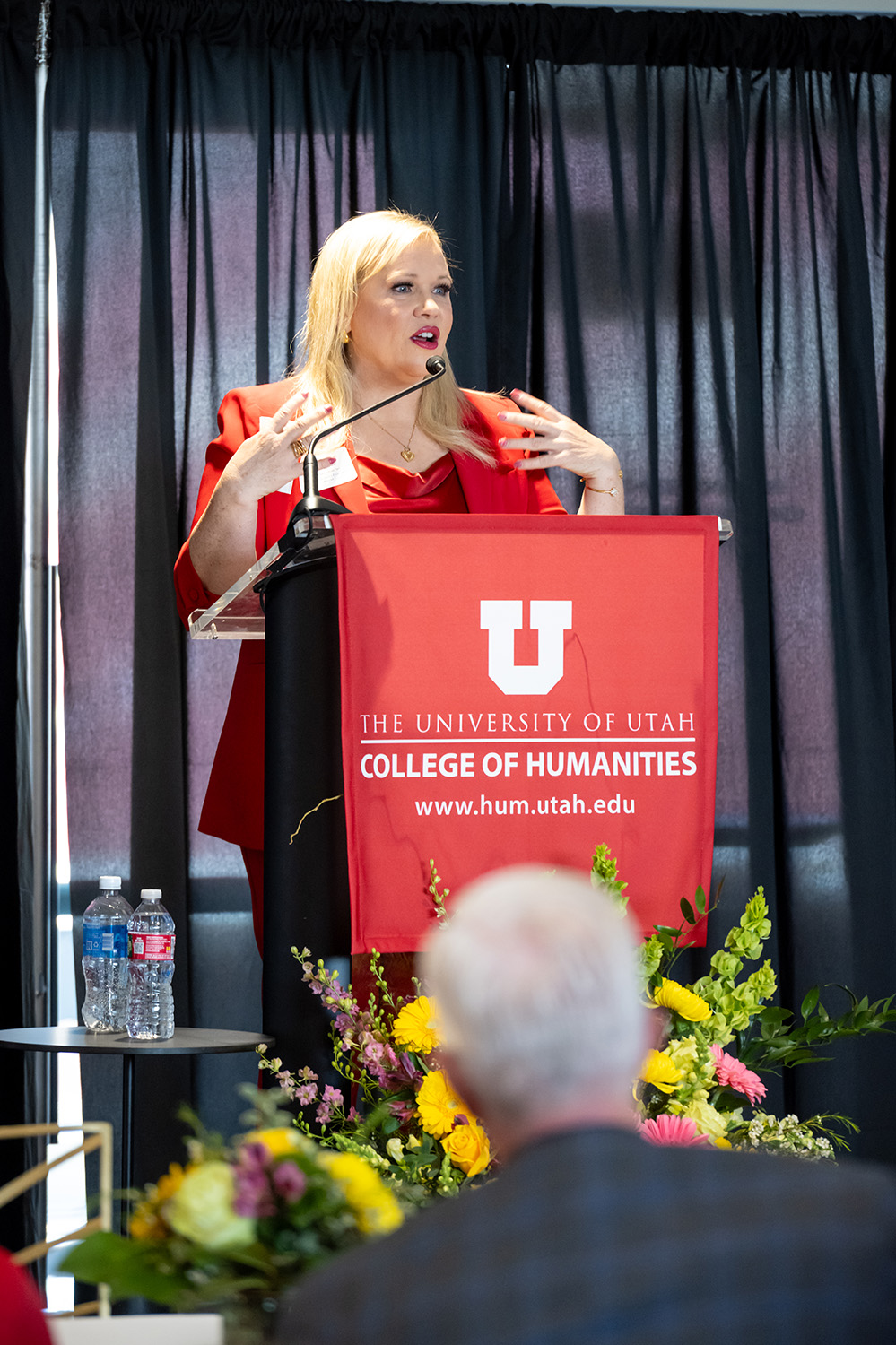 Holly Rowe speaks from behind a podium draped with a College of Humanities banner