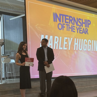 Marley accepting award with a screen displaying her name in the background
