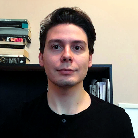 Headshot of Aniello smiling at the camera and stacks of books in the background