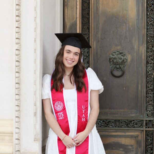 Young woman with wavy hair with a white dress U of U red stole and black graduation cap.