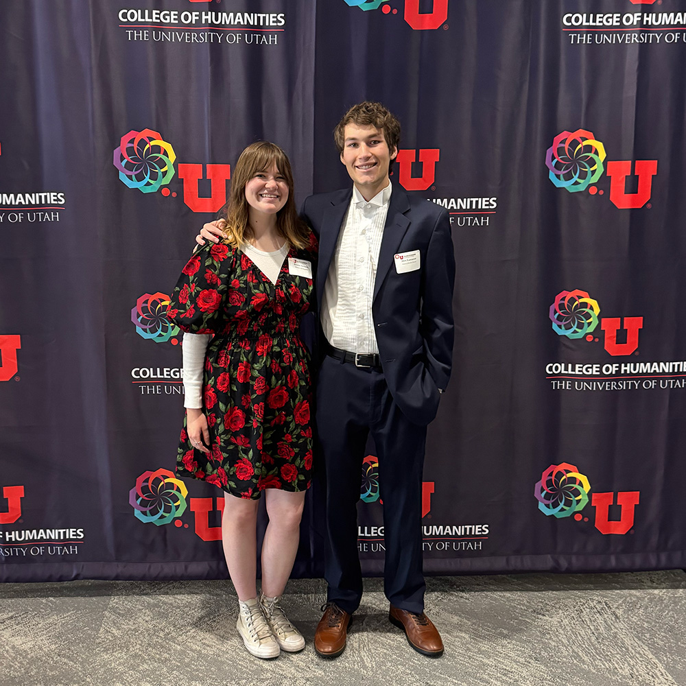 Brooke stands on the left. A young man has an arm around her and side to her right.