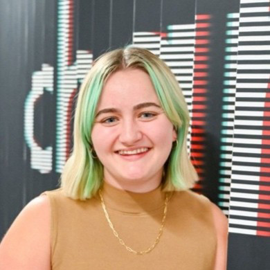 Young woman with short blonde green hair smiles at the camera