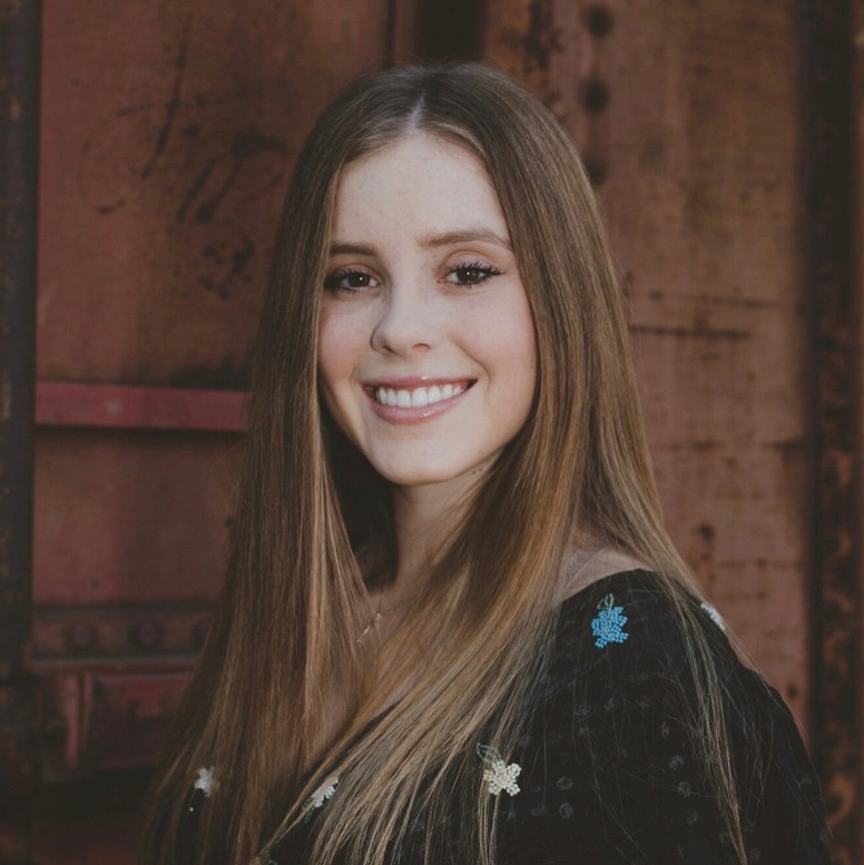 Young woman with straight brown hair and floral blouse smiling at the camera