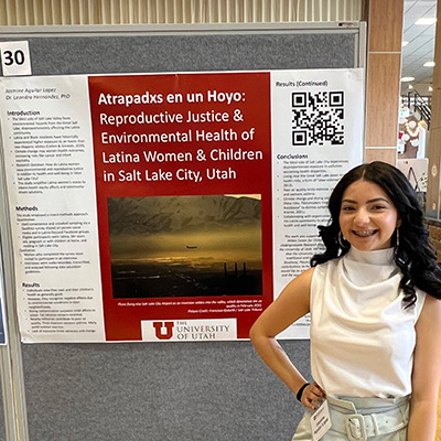 Jasmine smiling at the camera with her research poster in the behind her
