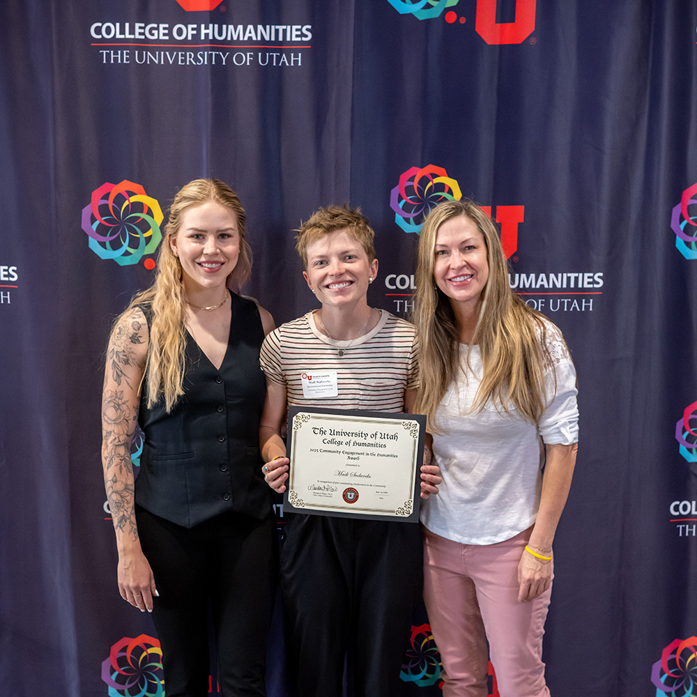 3 young women stand together. The one in the middle is holding an award