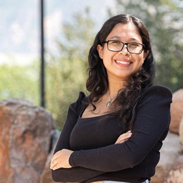 A young woman with black rim glasses and black long sleeve smiling at the camera.