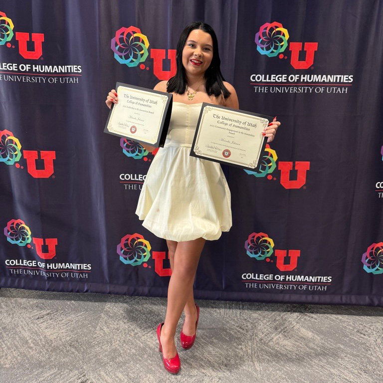 A young woman in white dress holding 2 awards