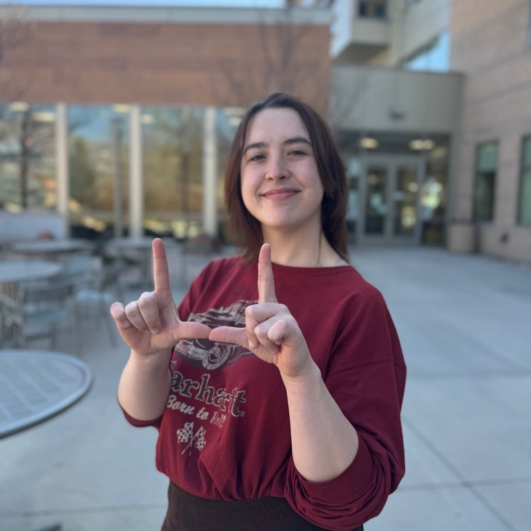 A young woman in a maroon sweater flashing the U with her hands
