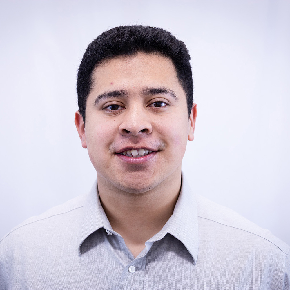 Young man with short dark hair wears a light gray buttondown as he smiles at the camera