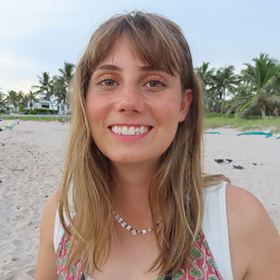 Ashlyn smiling at the camera with a white sand beach as the background. 