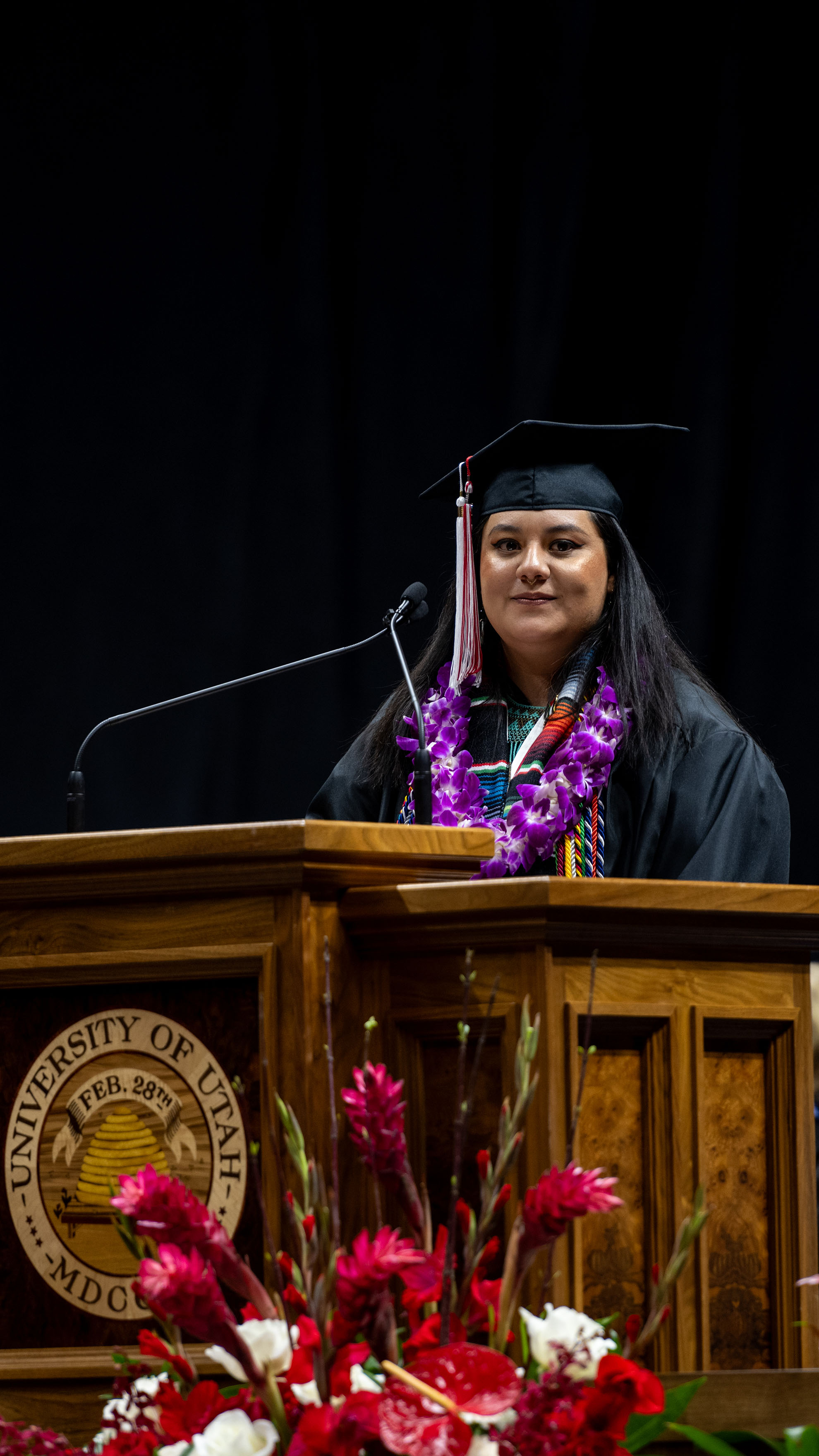 Evelyn in her graduation regalia standing on stage behind the podium giving her speech